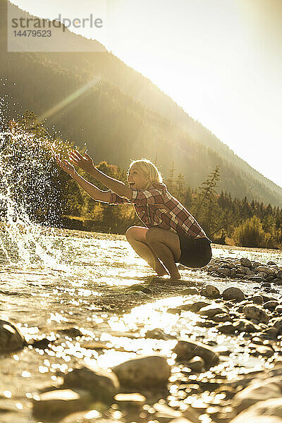 Österreich  Alpen  glückliche Frau auf Wanderung  die an einem Bach mit Wasser spritzt