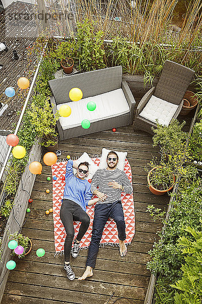 Junges Paar entspannt sich auf dem Balkon  auf einer Decke liegend und die Arme um den Körper gelegt