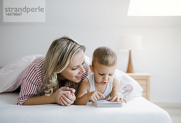 Lächelnde Mutter und Kleinkind-Sohn liegen zu Hause im Bett und lesen ein Buch