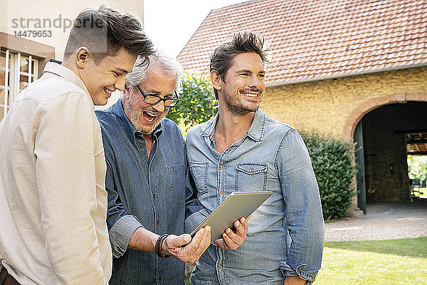 Drei glückliche Männer unterschiedlichen Alters mit Tablette im Garten