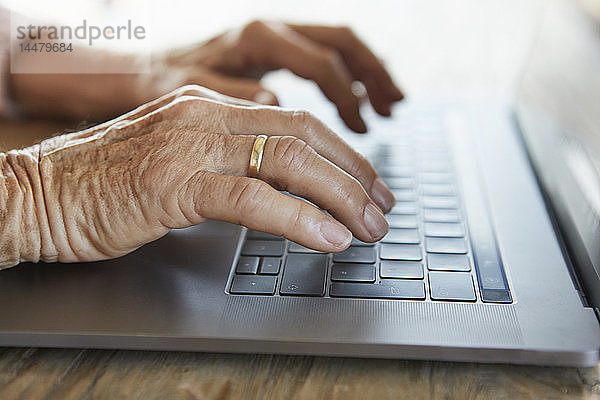 Hand einer älteren Frau beim Tippen auf der Tastatur eines Laptops  Nahaufnahme