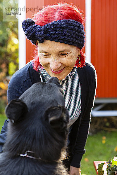 Porträt einer lächelnden älteren Frau mit rot gefärbtem Haar von Angesicht zu Angesicht mit ihrem Hund im Garten