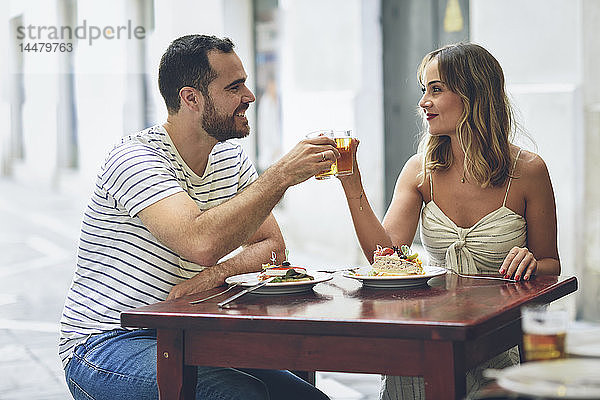 Lächelndes Paar klimpert Bier in einem Restaurant auf der Strasse