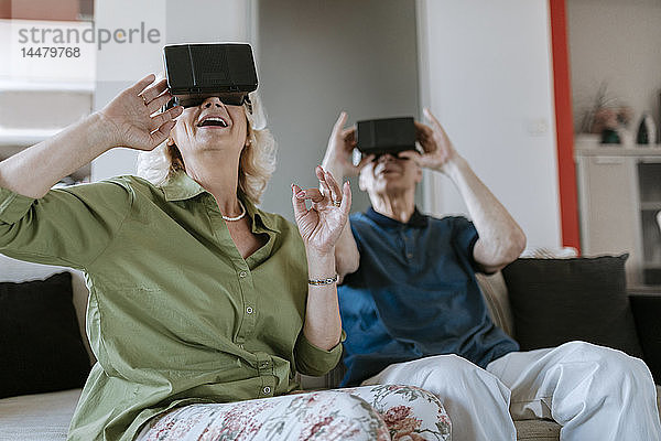 Glückliches älteres Ehepaar zu Hause  das mit einer VR-Brille auf der Couch sitzt