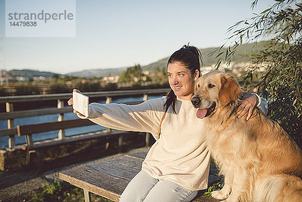 Lächelnde junge Frau  die mit ihrem Hund am Wasser einen Selfie mitnimmt