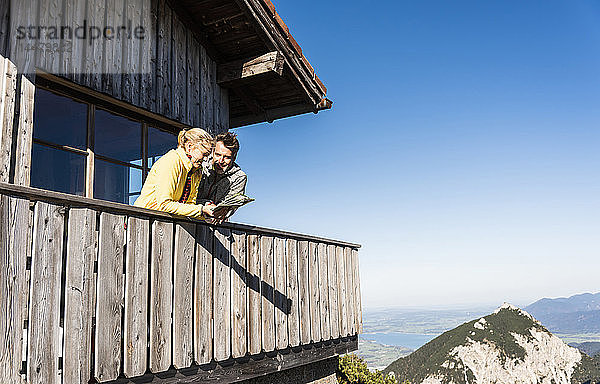 Paar lehnt auf dem Balkon einer Berghütte  hält Karte