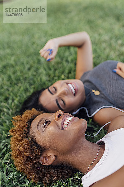 Porträt von zwei glücklichen Freundinnen  die sich in einem Park entspannen und Musik hören