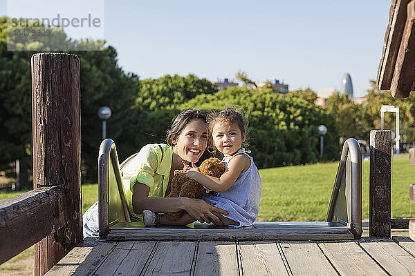 Lächelnde Mutter mit Tochter auf einer Rutsche auf einem Spielplatz