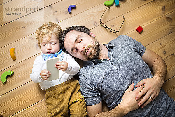 Vater liegt mit seinem kleinen Sohn auf dem Boden und spielt mit dem Smartphone