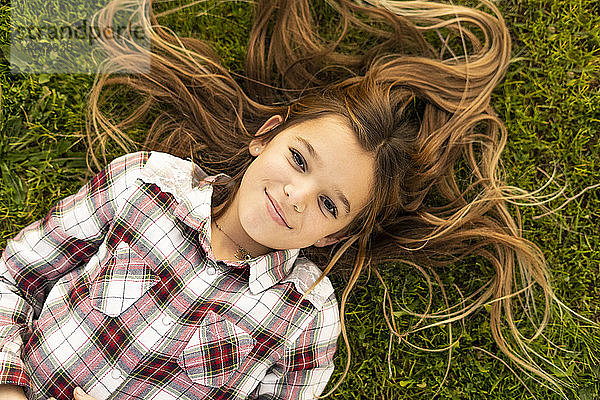 Bildnis eines lächelnden Mädchens mit langen Haaren auf einer Wiese liegend