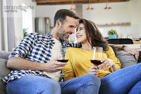 Glückliches Paar sitzt im Wohnzimmer und trinkt Rotwein