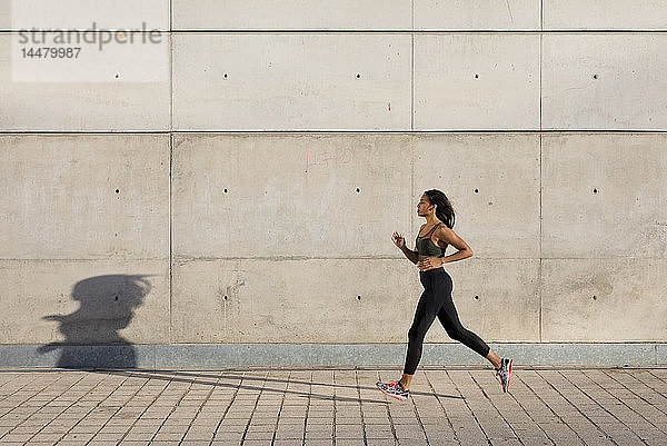 Junge Frau rennt entlang der Betonmauer in der Stadt