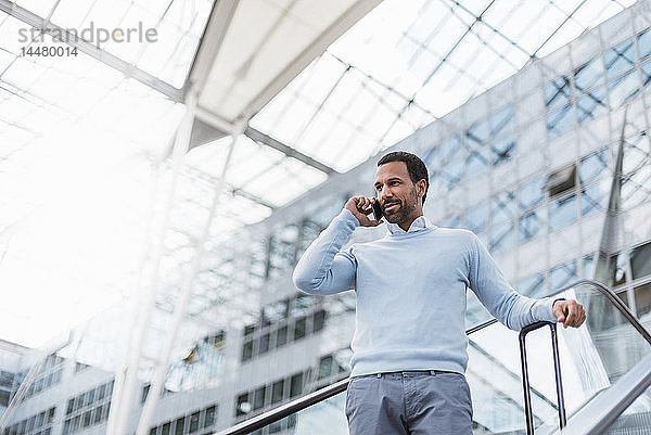 Geschäftsmann benutzt Smartphone auf Rolltreppe