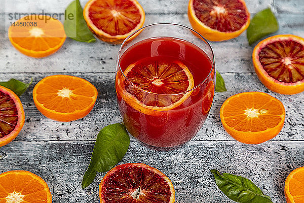 Glas Blutorangensaft und Hälften von Blutorangen und Mandarinen