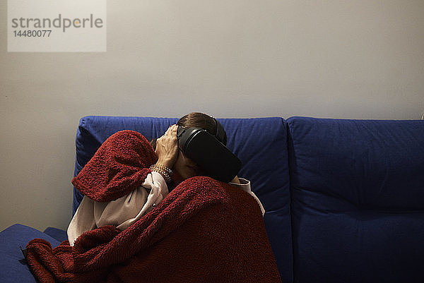 Verängstigte Frau  die nachts allein zu Hause ist und ein Virtual-Reality-Headset benutzt  um sich einen Film anzusehen.