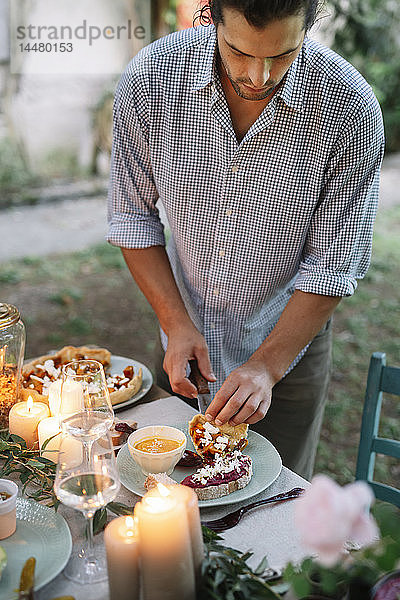 Mann arrangiert ein romantisches Essen bei Kerzenlicht im Freien