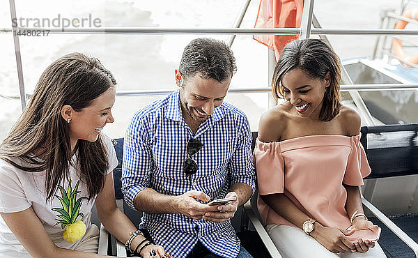 Großbritannien  London  glückliche Freunde  die während einer Schiffsreise auf der Themse ein Handy benutzen