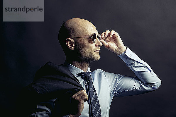 Porträt eines kahlköpfigen Geschäftsmannes mit Sonnenbrille vor schwarzem Hintergrund