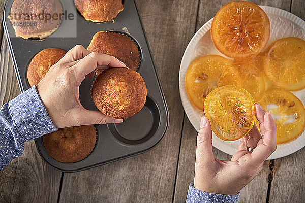 Frauenhände  die Muffins mit kandierten Orangenscheiben garnieren