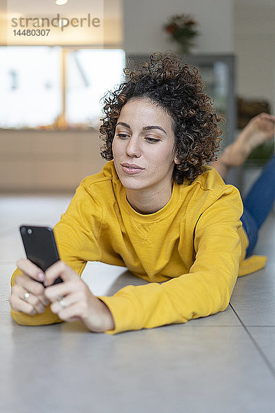 Frau liegt zu Hause auf dem Boden und benutzt ihr Handy