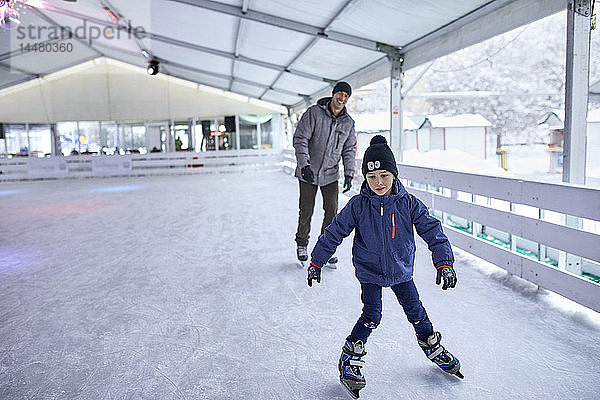 Vater und Sohn laufen gemeinsam Schlittschuh und haben Spaß auf der Eisbahn