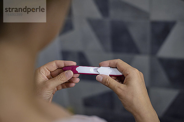 Nahaufnahme einer Frau  die ihren Schwangerschaftstest mit positivem Ergebnis überprüft