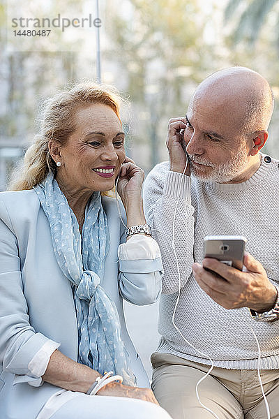 Spanien  Barcelona  glückliches älteres Ehepaar  das sich ein Smartphone mit Ohrstöpseln teilt