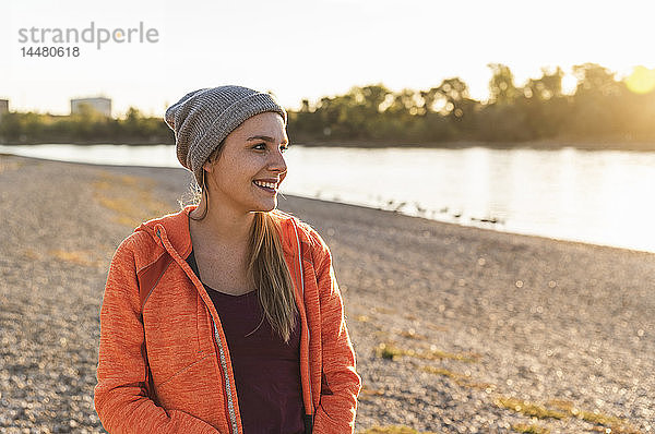 Porträt einer sportlichen jungen Frau am Fluss  die einen Mützenhut trägt
