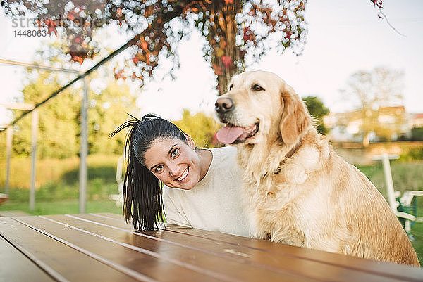 Porträt einer glücklichen jungen Frau mit ihrem Golden-Retriever-Hund  der sich in einem Park ausruht