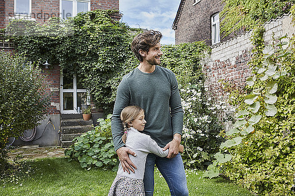 Lächelnder Vater mit Tochter steht im Garten ihres Hauses