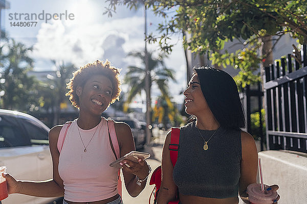 USA  Florida  Miami Beach  zwei glückliche Freundinnen mit Handy und Erfrischungsgetränk in der Stadt