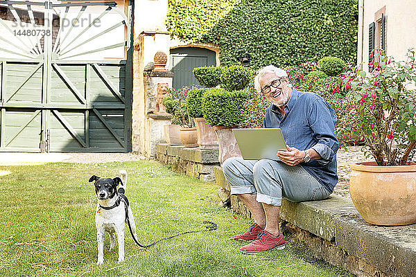 Porträt eines lachenden älteren Mannes mit Hund im Garten mit Tablette