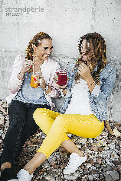 Zwei Freundinnen trinken Smoothies im Freien und amüsieren sich