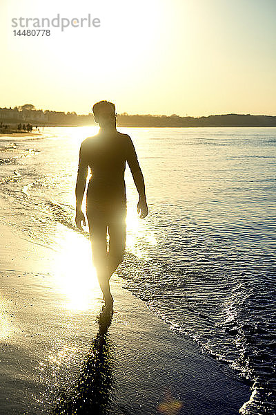 Silhouette eines Mannes  der bei Sonnenuntergang am Strand spazieren geht