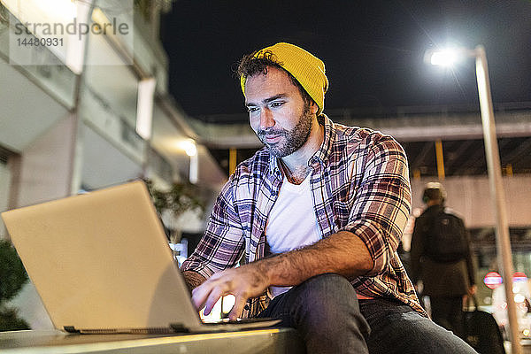 Großbritannien  London  lächelnder Mann mit Laptop nachts in der Stadt