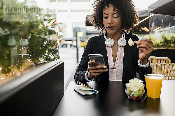 Porträt einer Geschäftsfrau  die im Straßencafé beim Essen von Obstsalat auf ihr Handy schaut