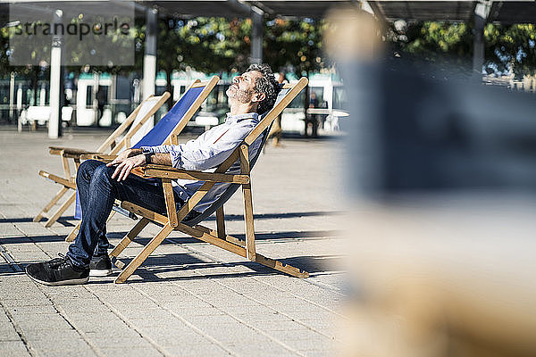 Reifer Mann entspannt sich im Liegestuhl auf einem Platz in der Stadt