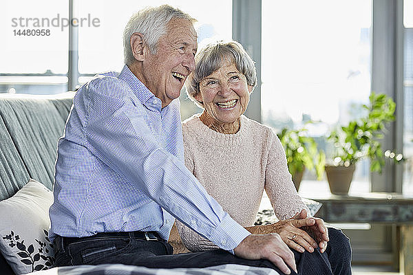 Porträt eines lachenden Seniorenpaares  das zusammen auf der Couch sitzt