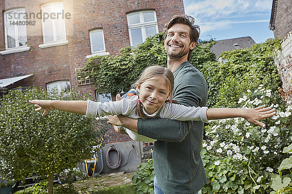 Glücklicher Vater spielt mit Tochter im Garten ihres Hauses