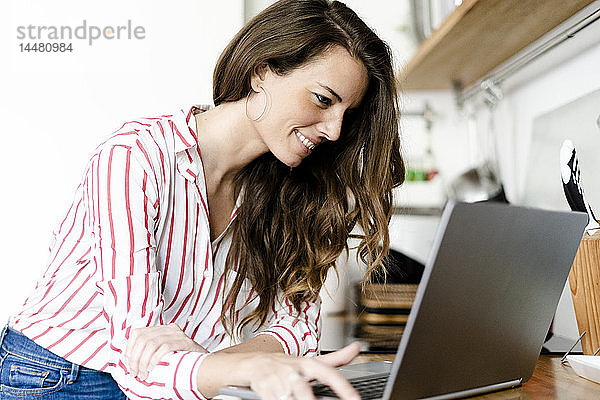 Lächelnde Frau benutzt Laptop in der Küche zu Hause