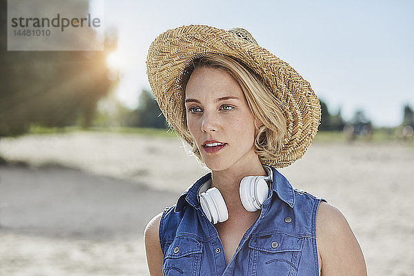 Porträt einer jungen Frau mit Kopfhörer und Strohhut am Strand