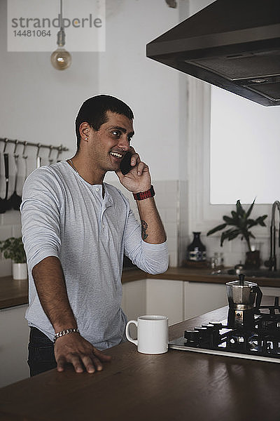 Lächelnder junger Mann am Handy in der heimischen Küche