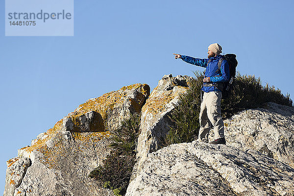 Spanien  Andalusien  Tarifa  Mann auf Wanderung  steht auf einem Felsen und zeigt mit dem Finger