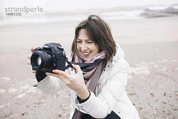 Porträt einer entspannten Frau  die am Strand mit der Kamera fotografiert