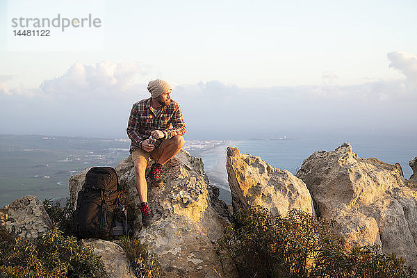 Spanien  Andalusien  Tarifa  Mann auf einer Wanderung an der Küste auf einem Felsen sitzend
