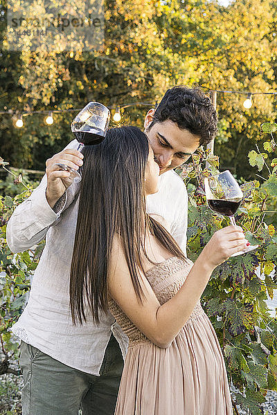 Italien  Toskana  Siena  liebevolles junges Paar mit Rotweingläsern in einem Weinberg