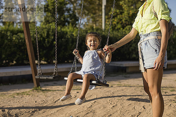 Mutter hält die Hand ihrer Tochter auf einem Spielplatz schwingend