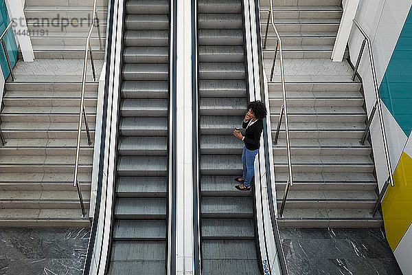 Geschäftsfrau am Telefon  die auf der Rolltreppe steht