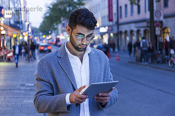 Deutschland  München  junger Geschäftsmann mit digitalem Tablet in der Stadt in der Abenddämmerung