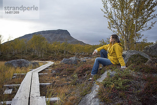 Finnland  Lappland  Kilpisjaervi  Frau an Holzpromenade sitzend